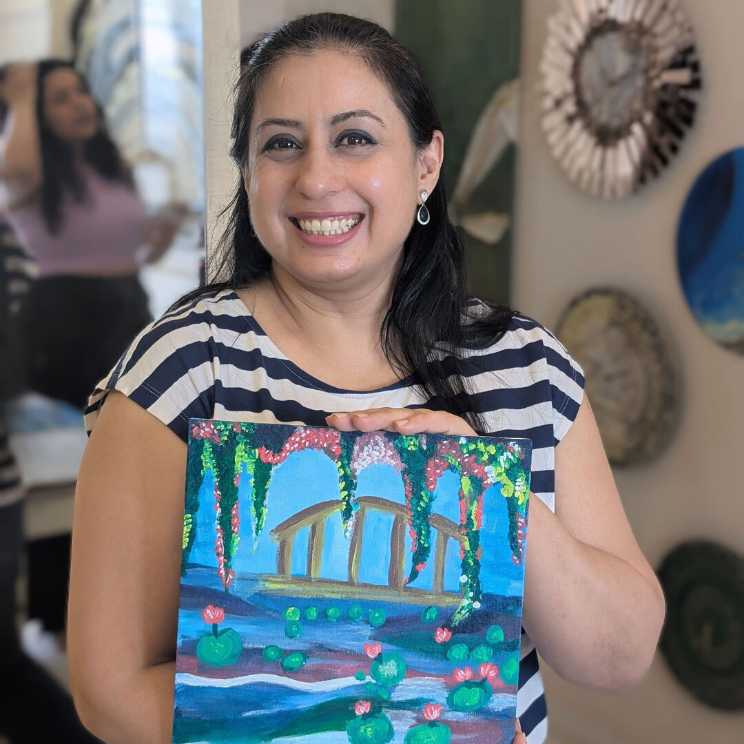 Smiling woman proudly holding her beginner-friendly painted canvas in a sip and paint session.