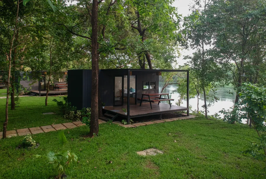 Cozy cabin with a riverside view surrounded by green trees and grass in pet-friendly camping area.