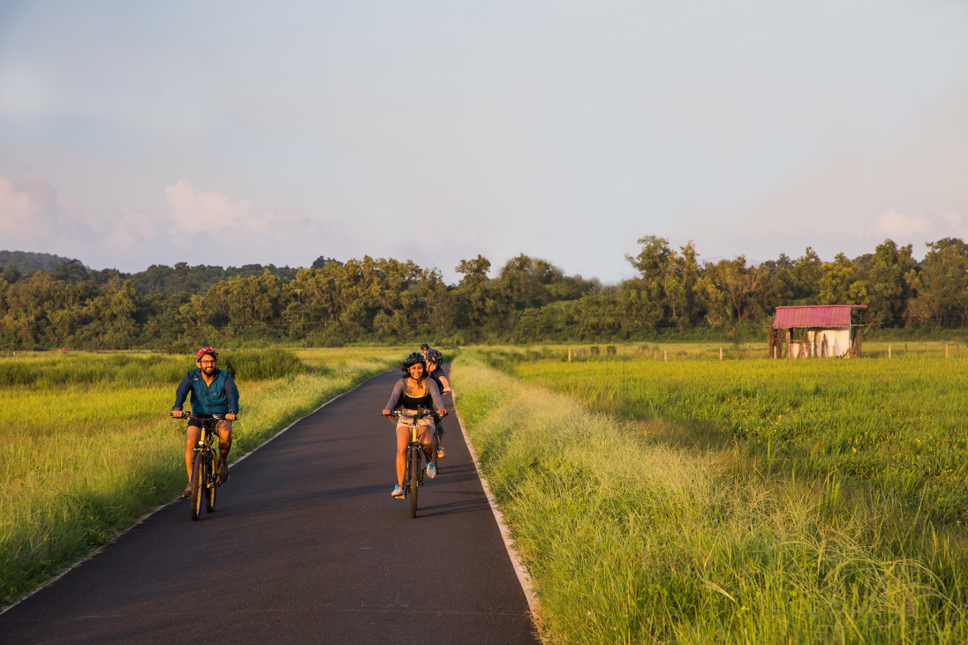 Two cyclists riding along a rural road with green fields on the Old Goa to Divar Island E-Bike Discovery Trail.