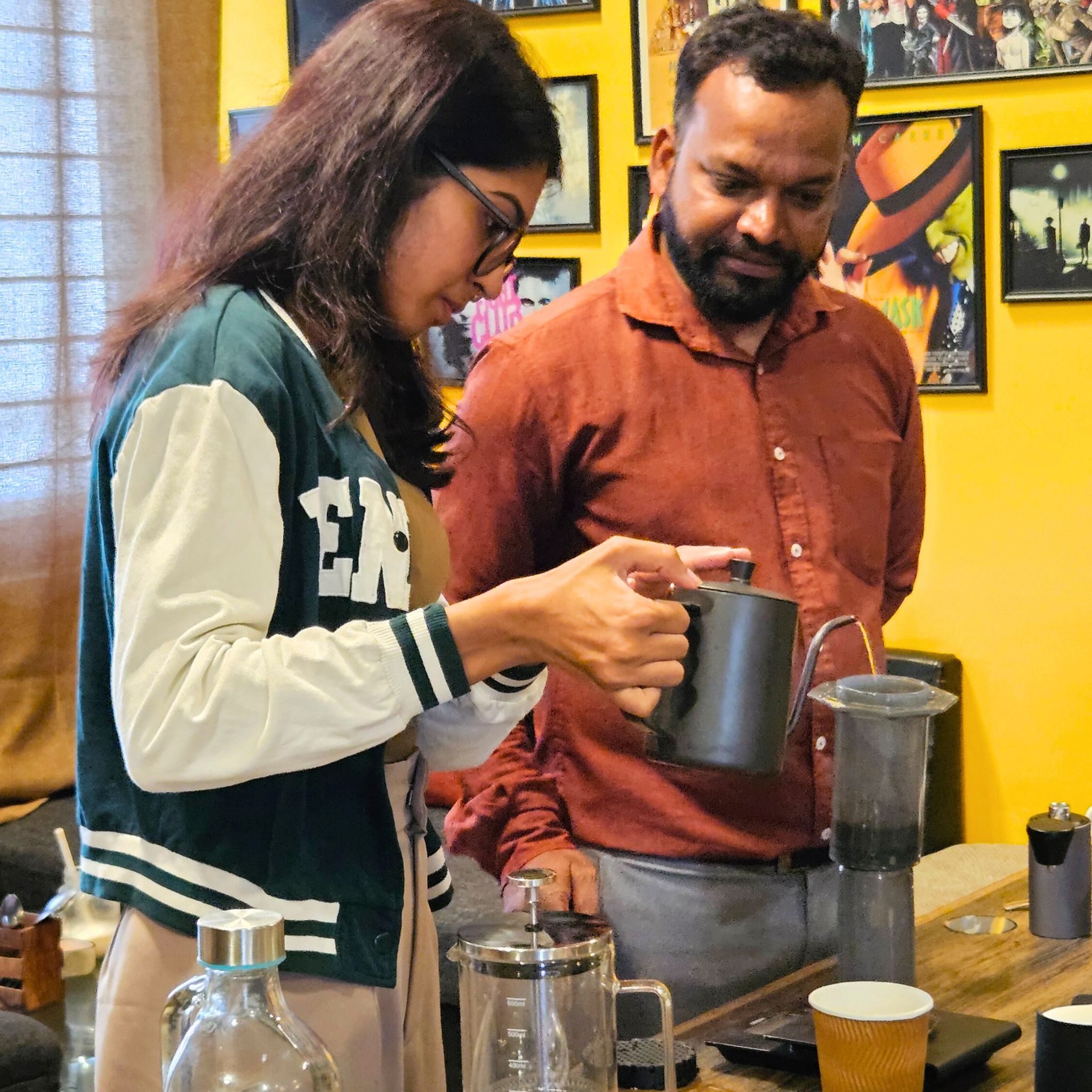 Woman pouring hot water from a kettle during a hands-on coffee brewing experience while a man observes.