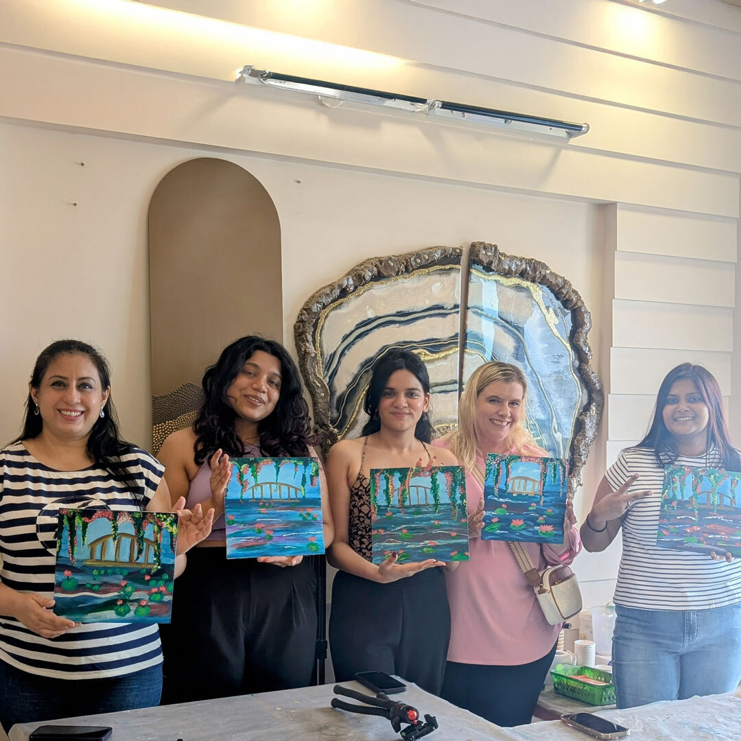 Group of five participants showing their completed colorful paintings, happy with their sip and paint creations.