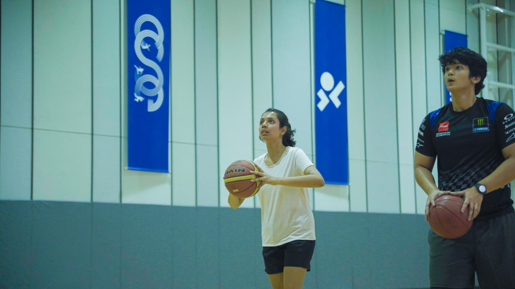 Female player preparing to shoot basketball with a male player standing beside on indoor court.