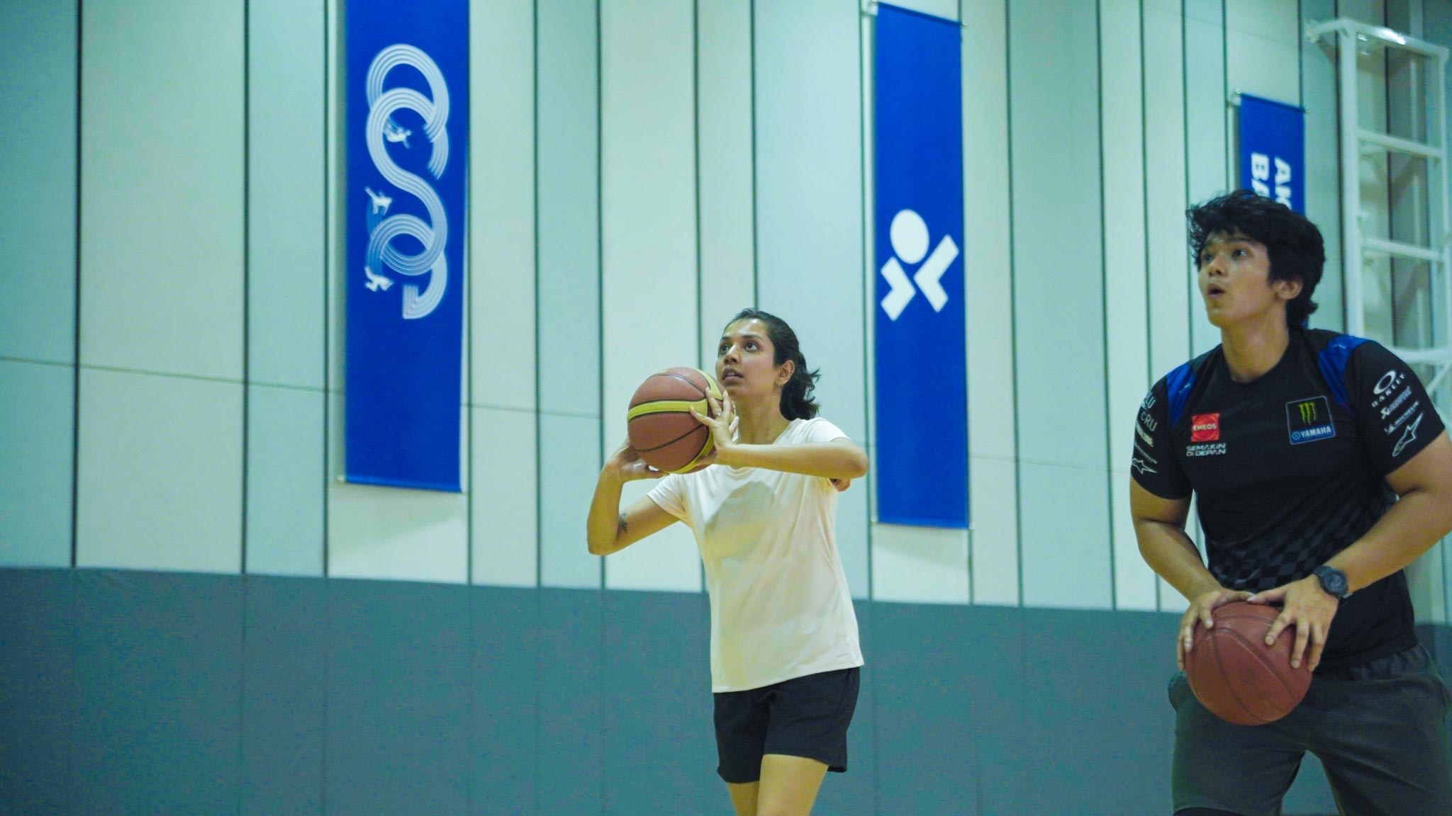 Two young men on indoor basketball court holding basketballs, getting ready to play in Bengaluru.