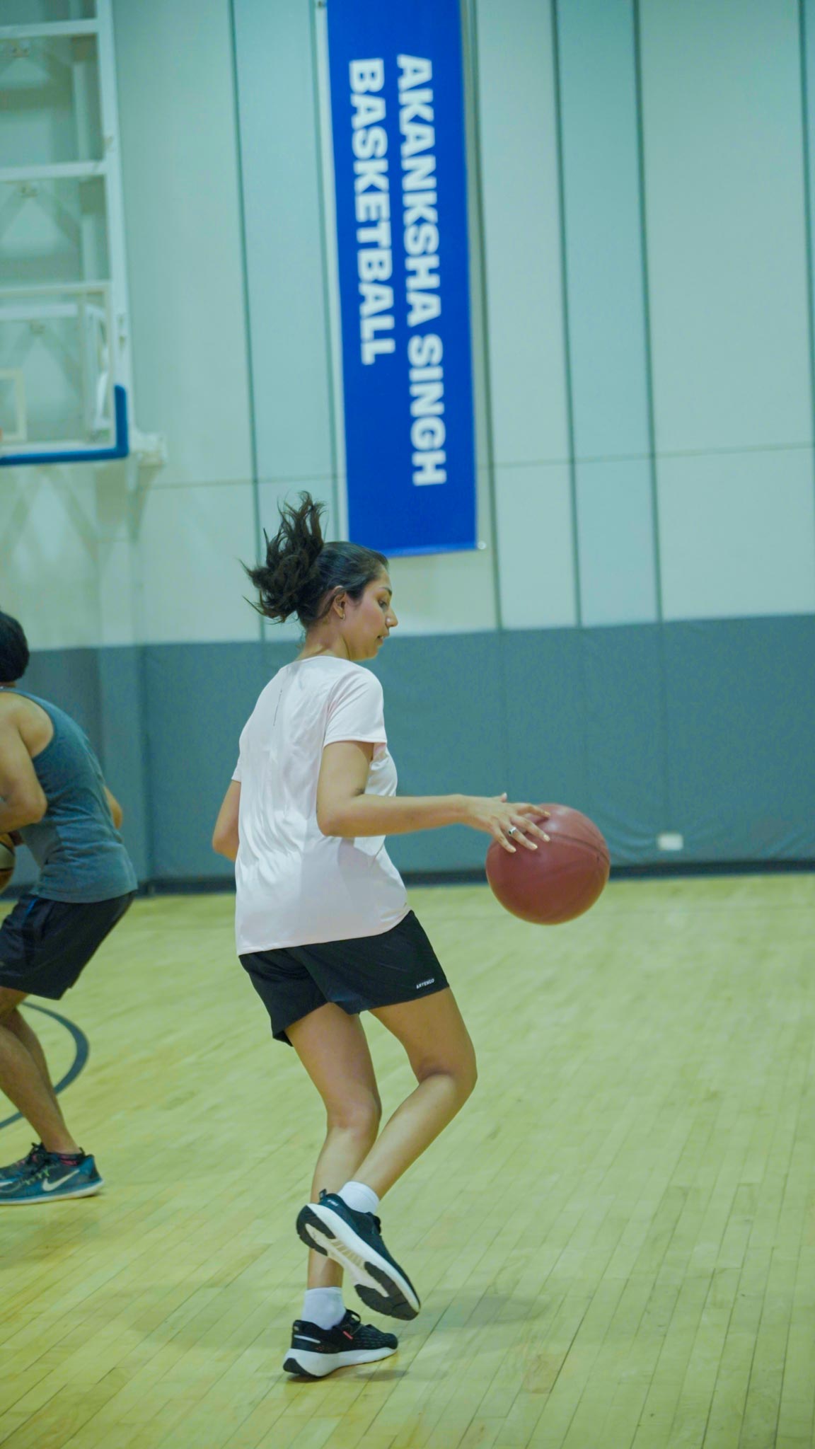 Female player dribbling basketball on indoor court named Akanksha Singh Basketball in Bengaluru.