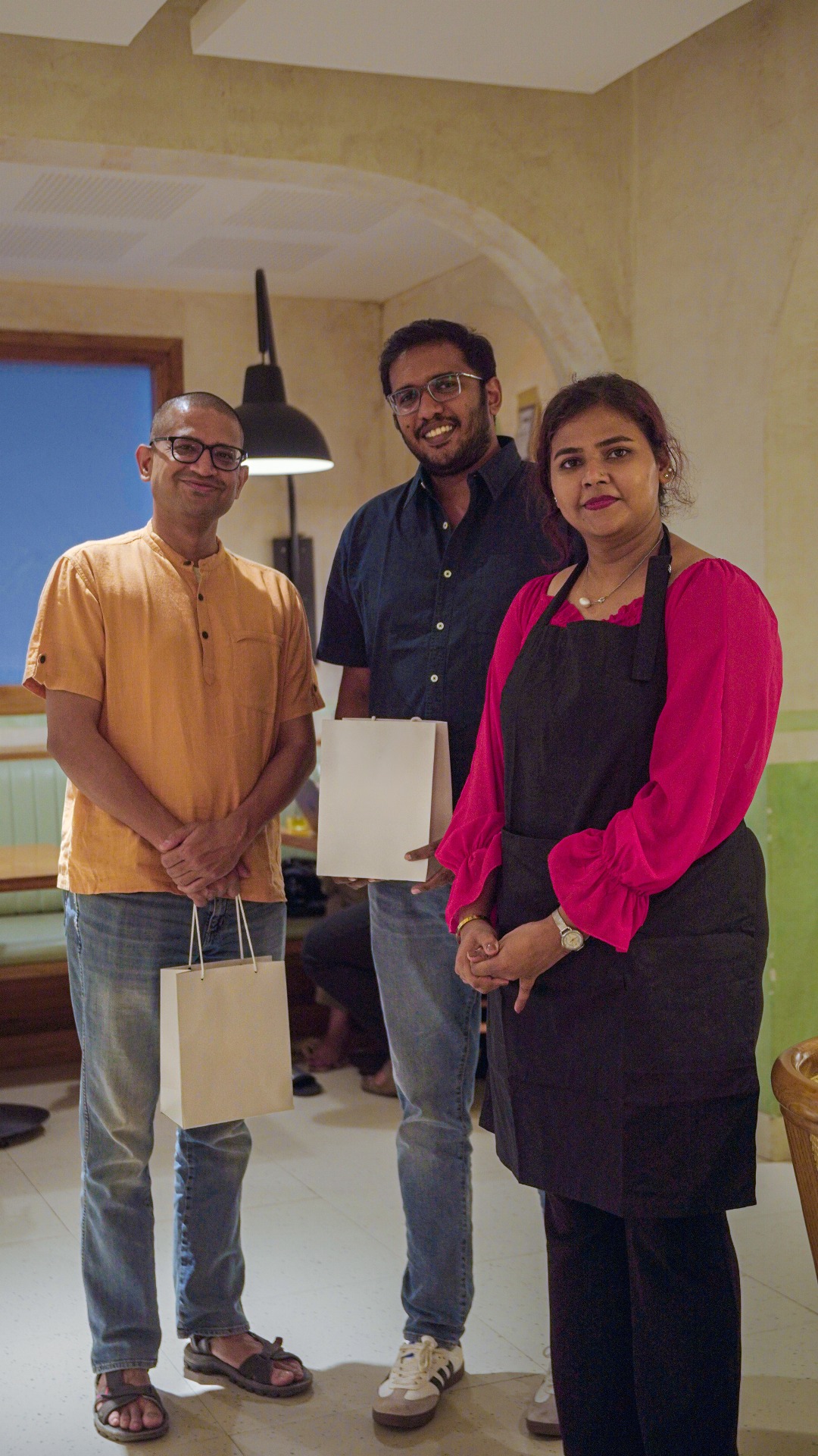 Three people smiling indoors, one wearing an apron, representing coffee experts or participants in a coffee brewing workshop in Hyderabad.