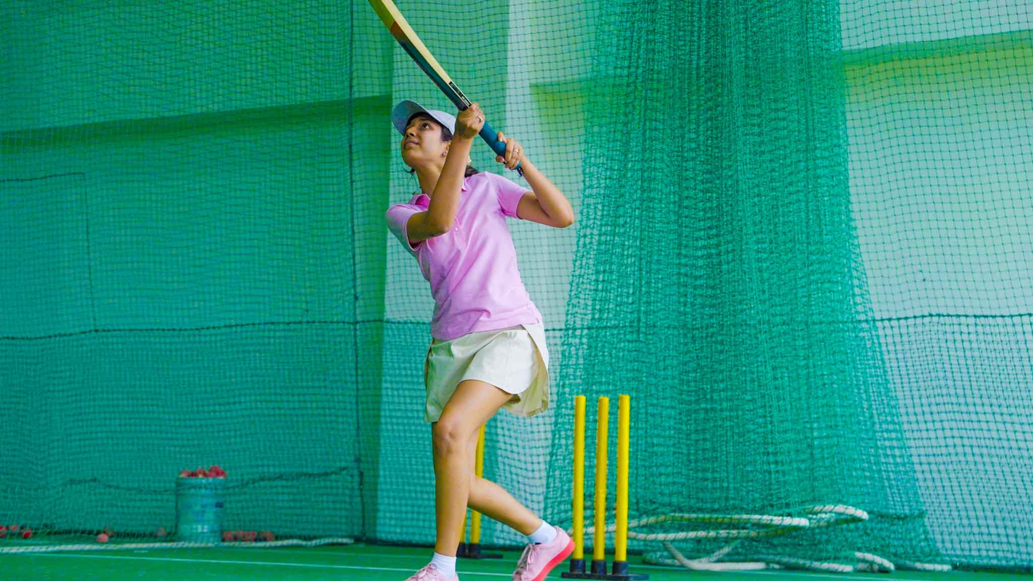 Woman holding cricket bat ready to play a shot in net practice.