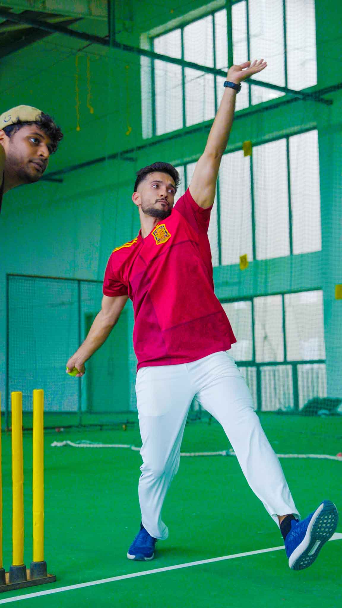 Man bowling cricket ball with focus in an indoor training facility.
