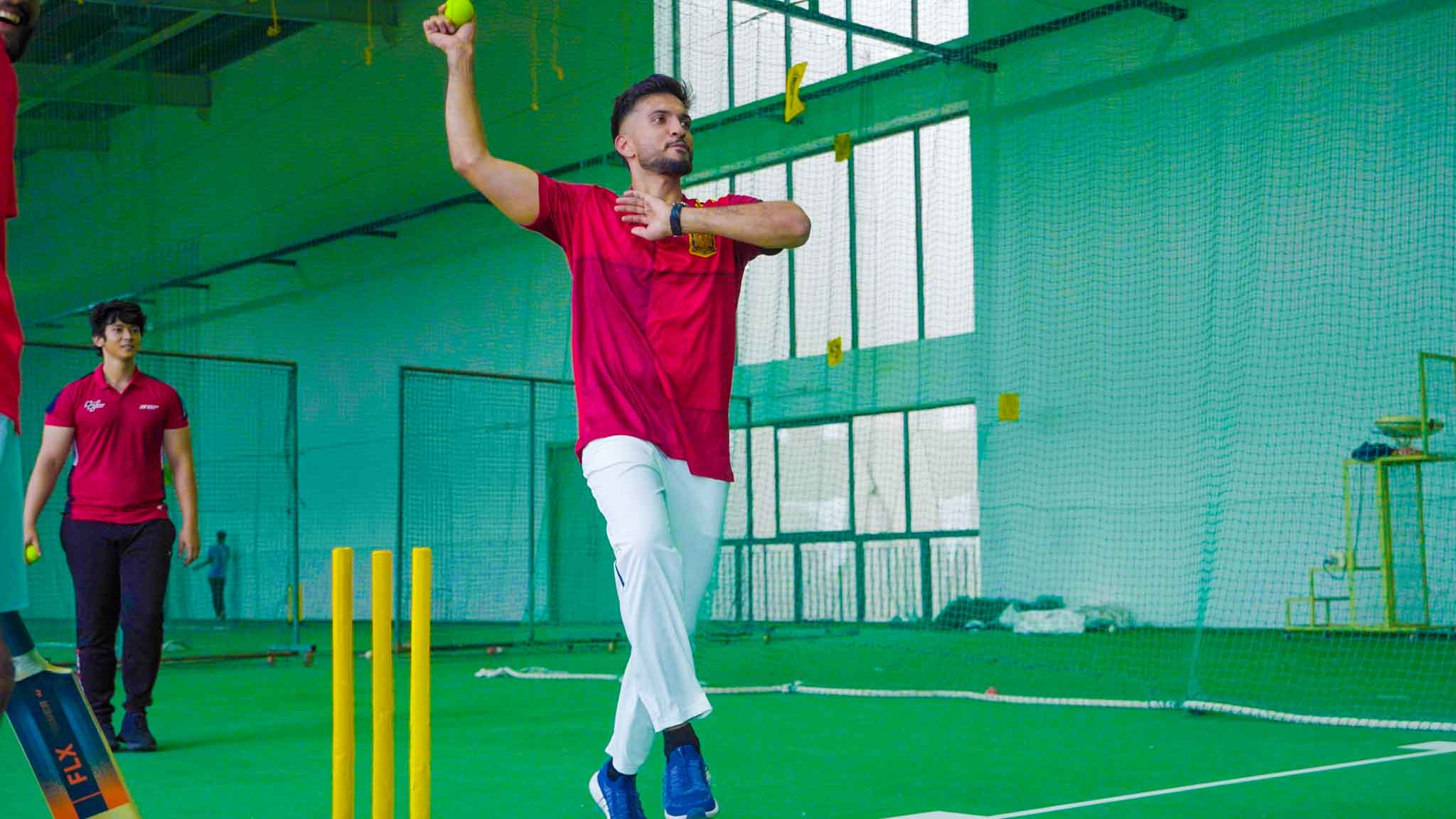 Man preparing to throw cricket ball in an indoor cricket facility.
