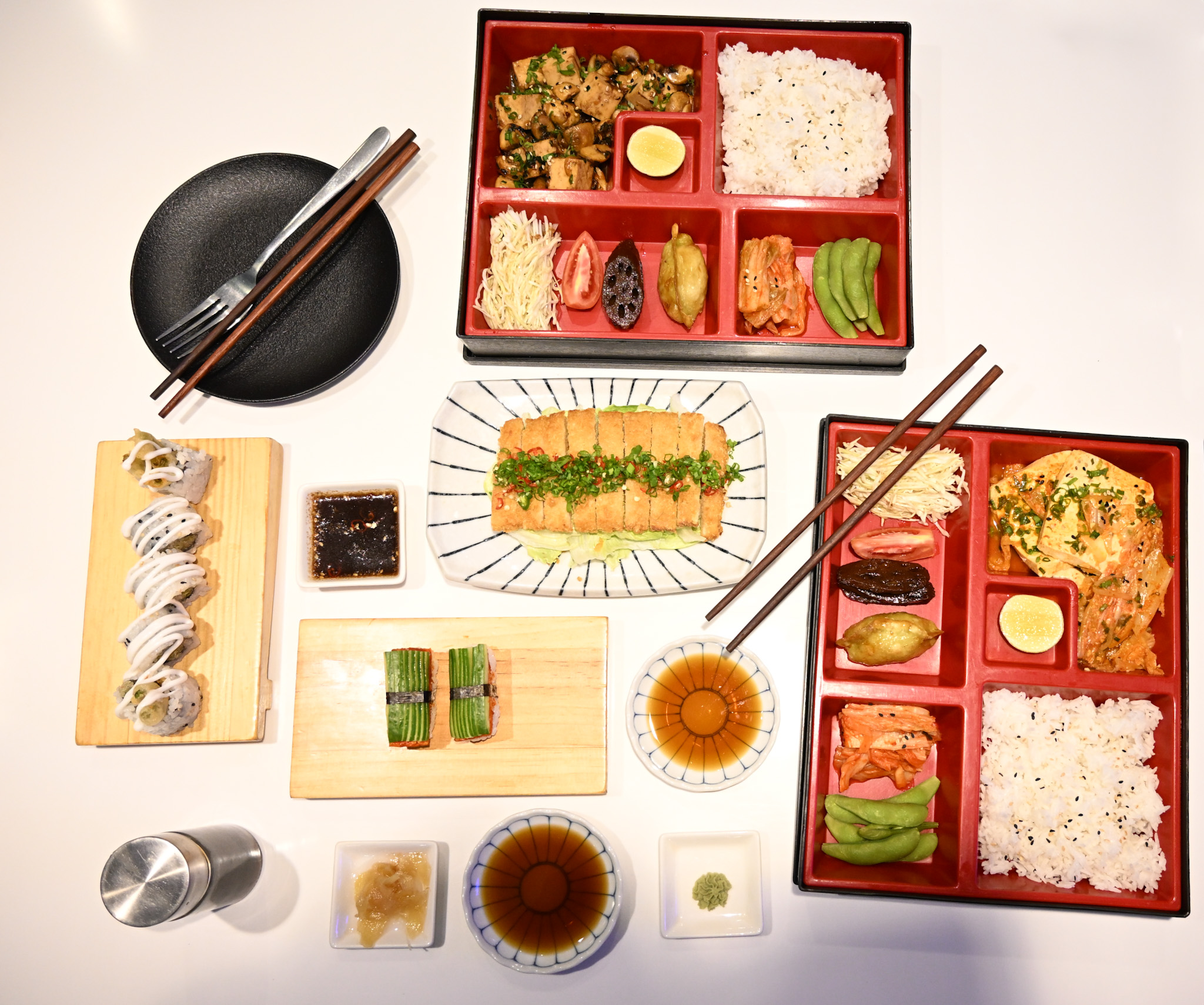 Overhead view of authentic Japanese dishes arranged on table including sushi, tempura and bento boxes.