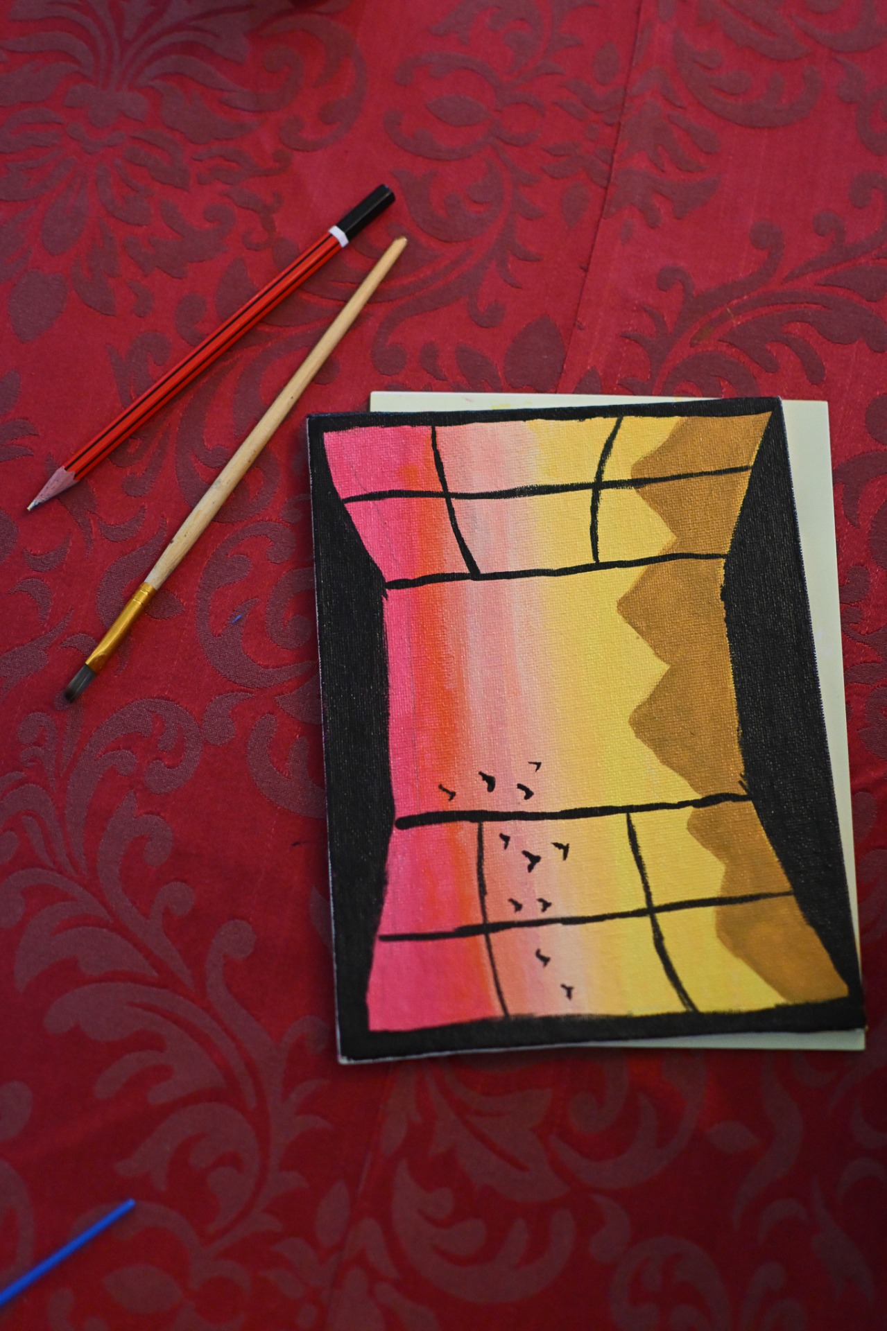 Sunset-inspired acrylic painting on canvas with brushes on red tablecloth during painting session.