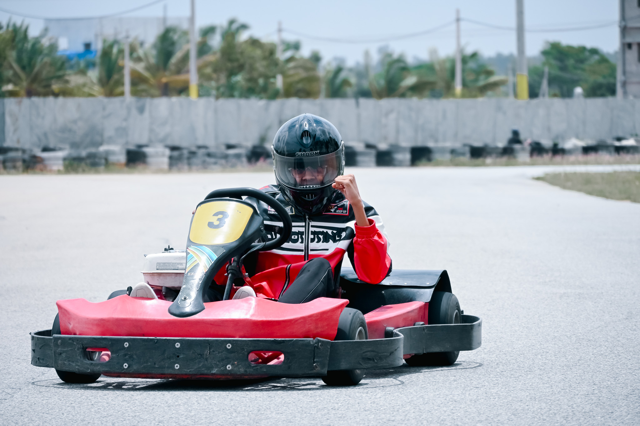 Person in a red and black jacket celebrating a win while driving a red go-kart on a race track in Bengaluru.