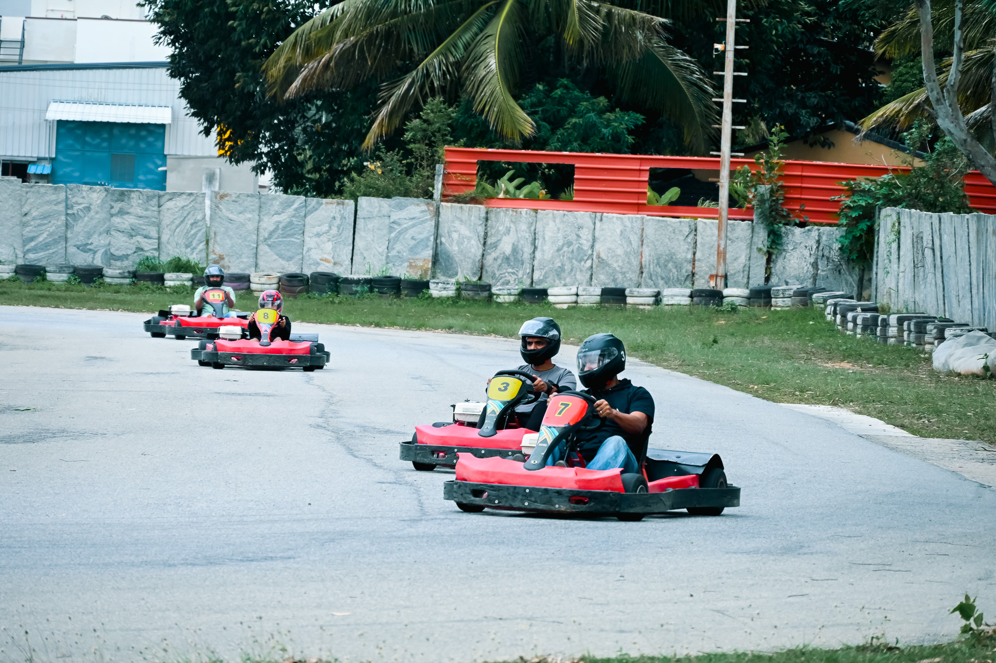 Group of four people driving red go-karts wearing helmets on an outdoor track in Bengaluru.