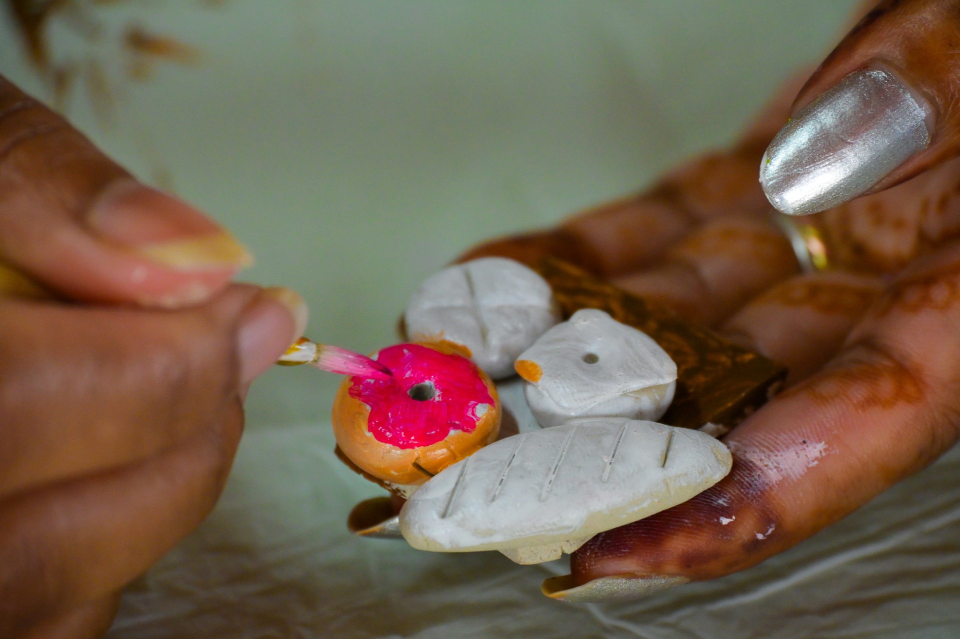 Close-up of hands painting delicate details on small clay pieces for magnets.
