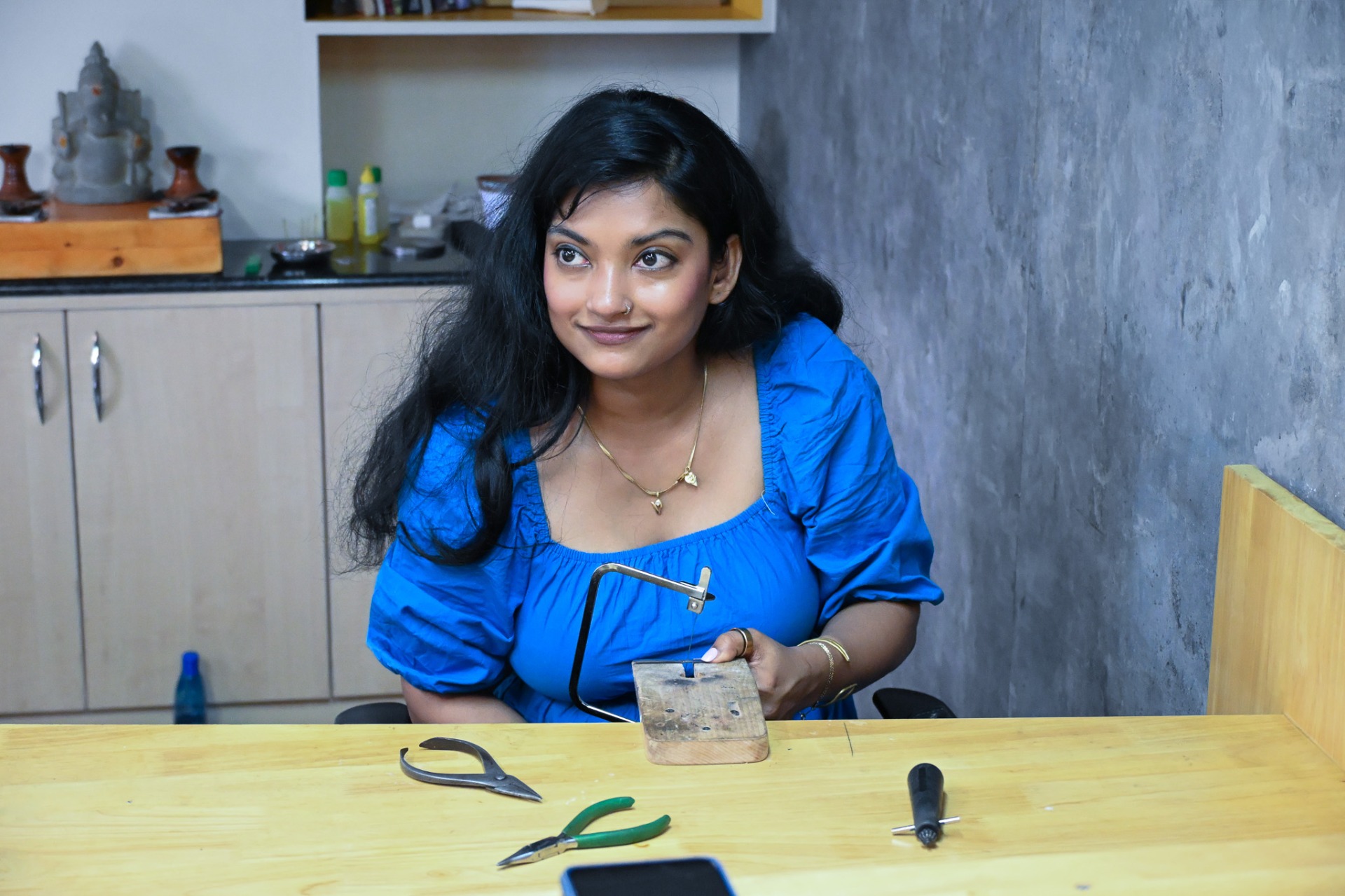 Woman holding jewelry saw frame with tools on the table during silver jewellery making class.