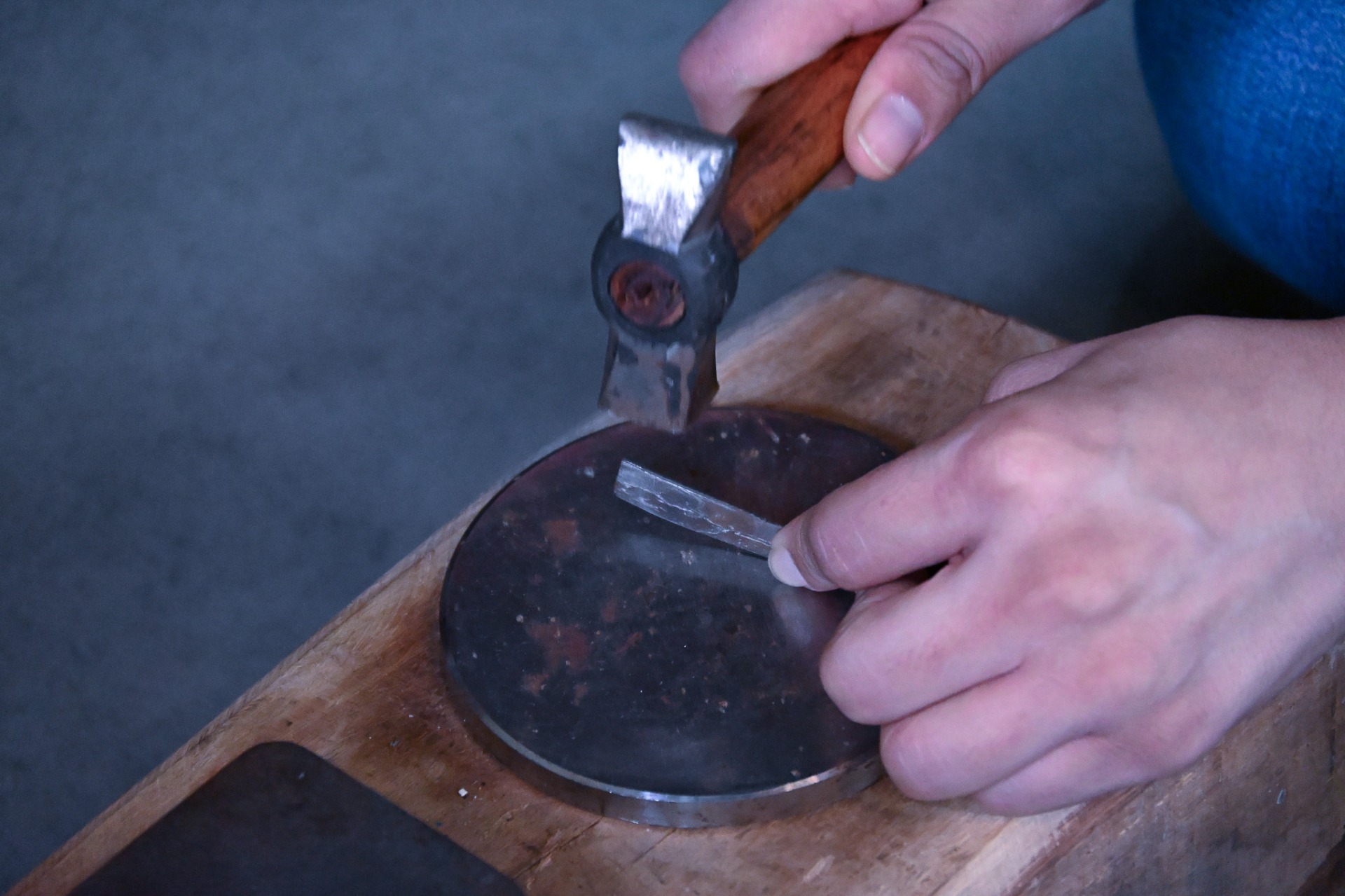Close-up of hands hammering a piece of silver metal on an anvil during jewellery crafting.