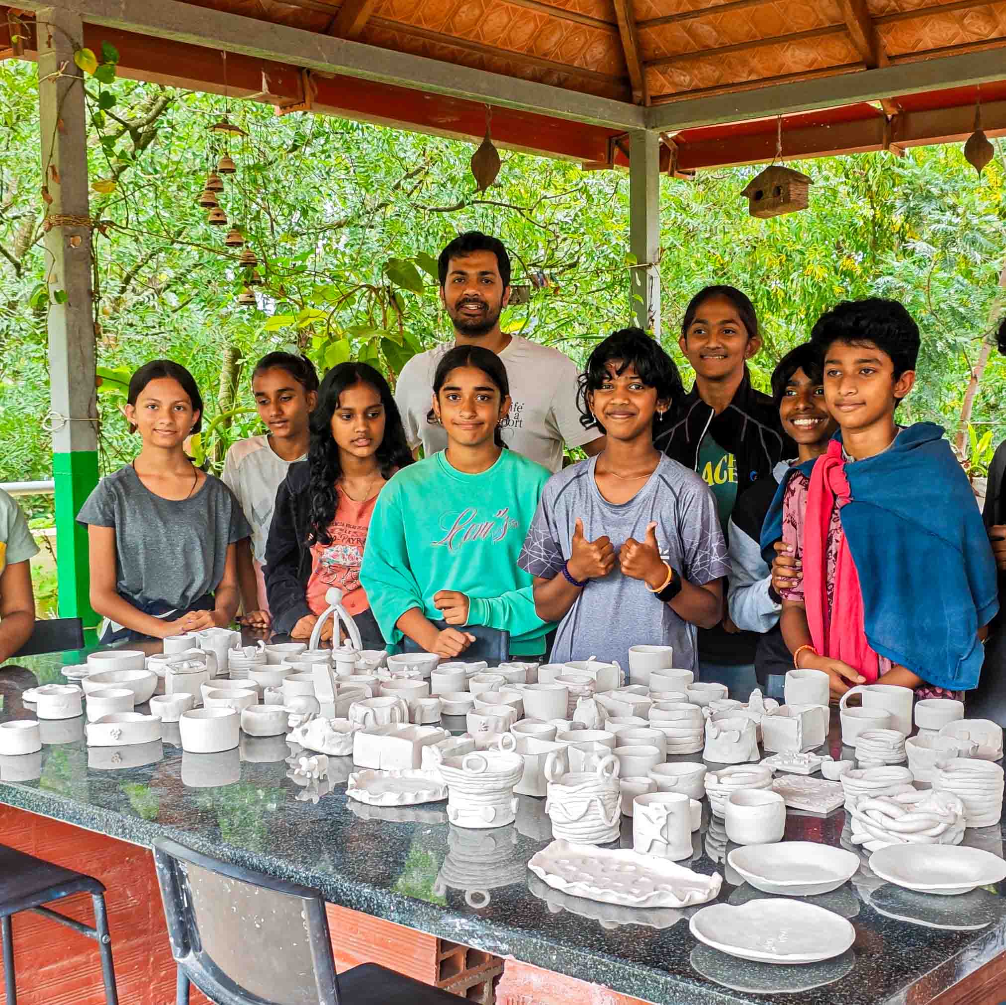 Pottery mentor posing with a group of young pottery learners and their creations.
