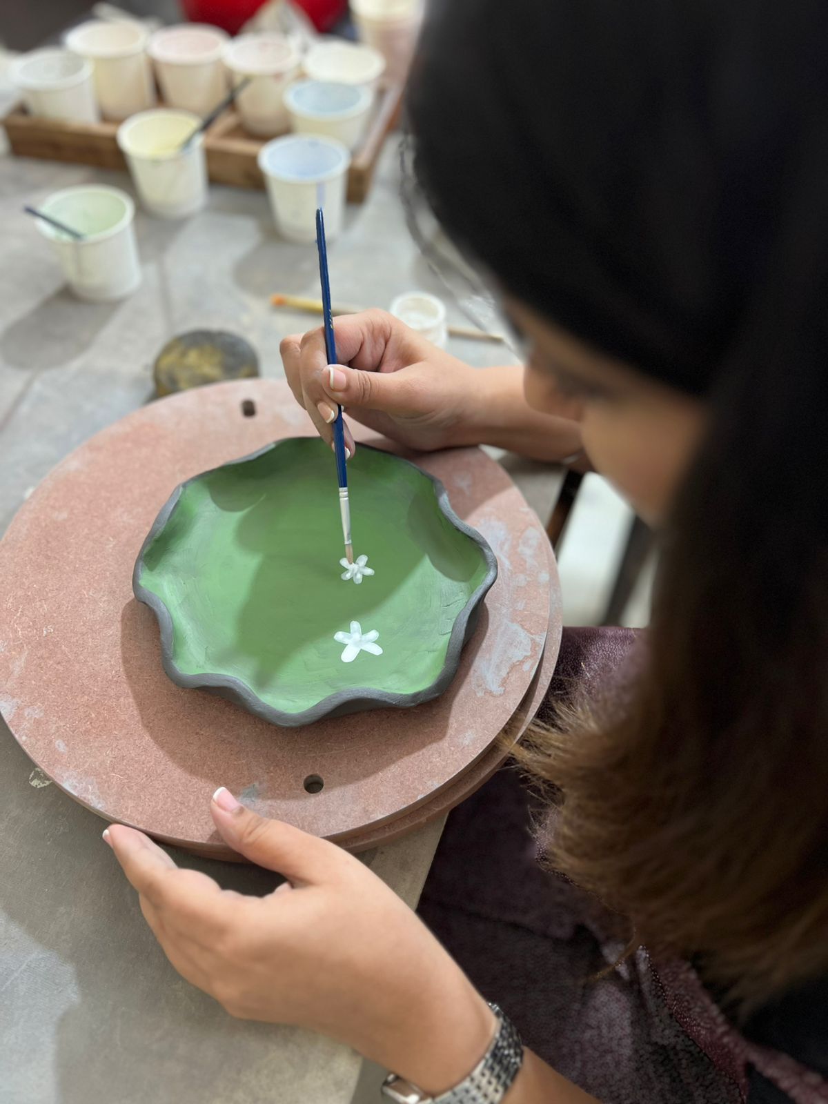 Participant painting small white flowers on a green pottery plate during Mumbai workshop.