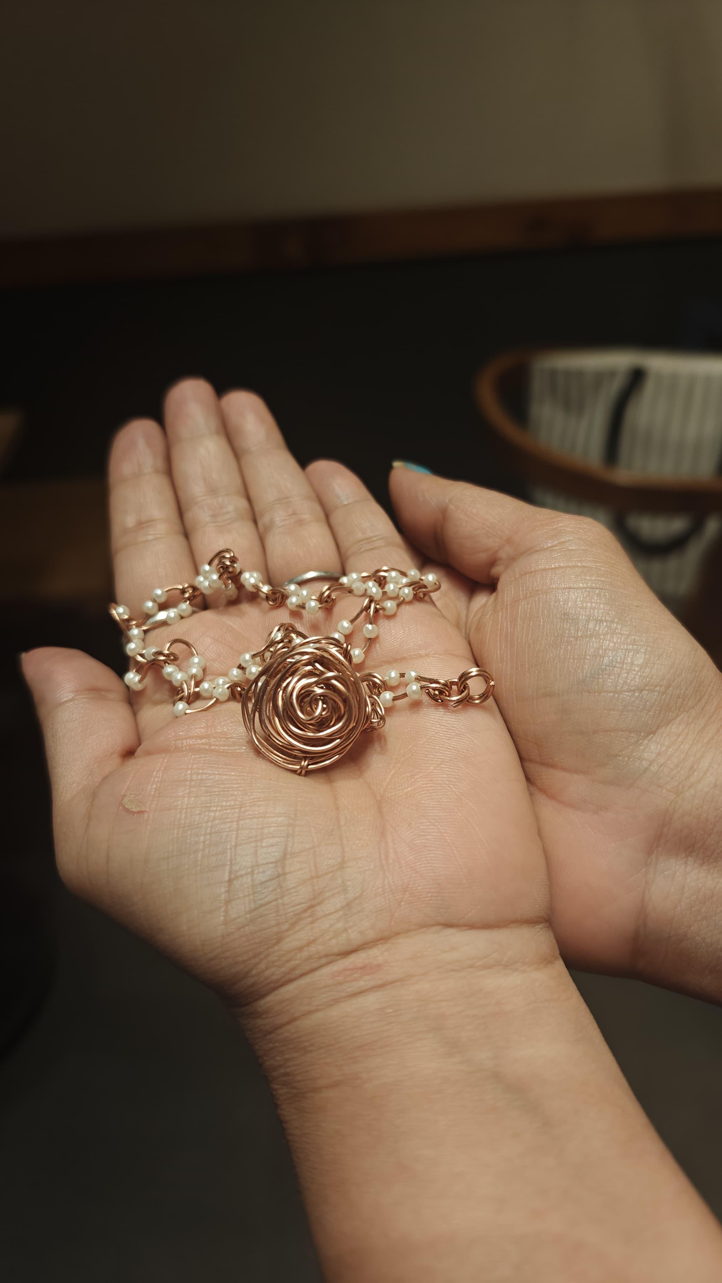 Hand holding a delicate handmade silver wire necklace with small pearls, showcasing finished jewelry piece.