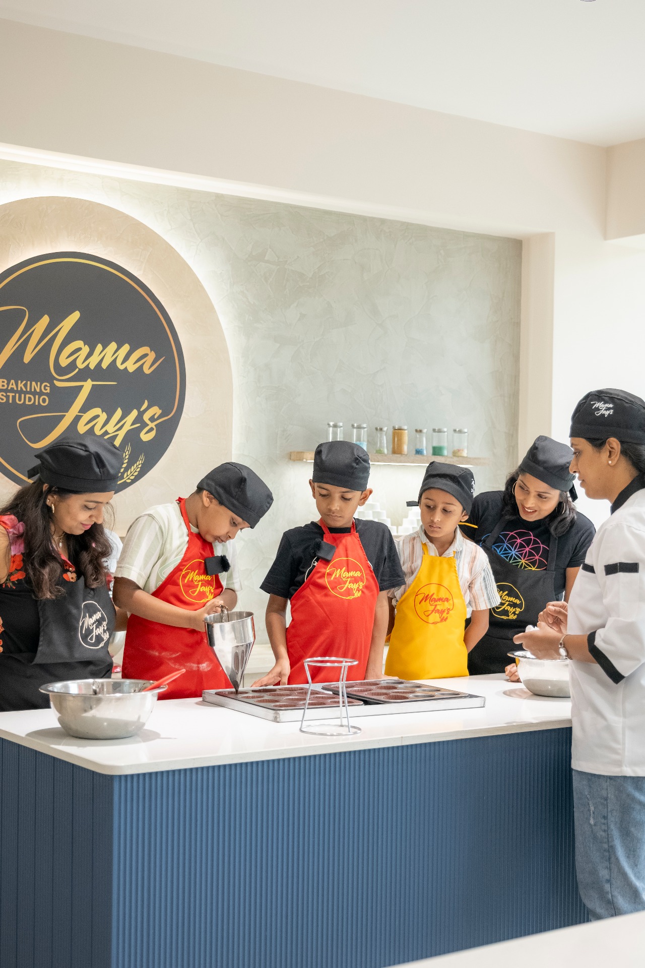 Group of kids with chef hats and aprons gathered around table learning baking with instructor at Mama Jay's.