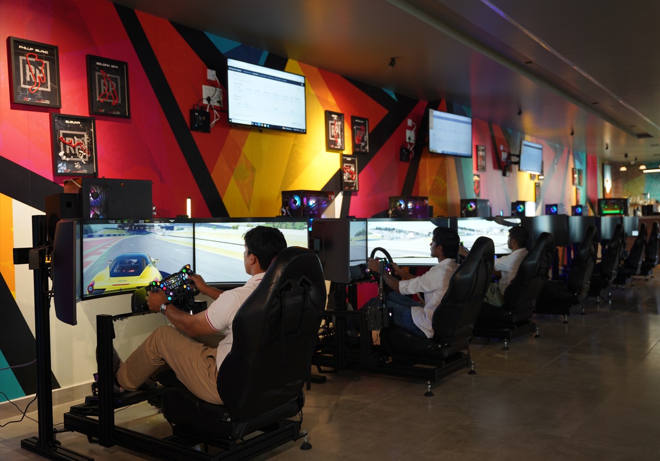 People racing on professional triple-screen simulators with steering wheels and pedals in a vibrant gaming setup.