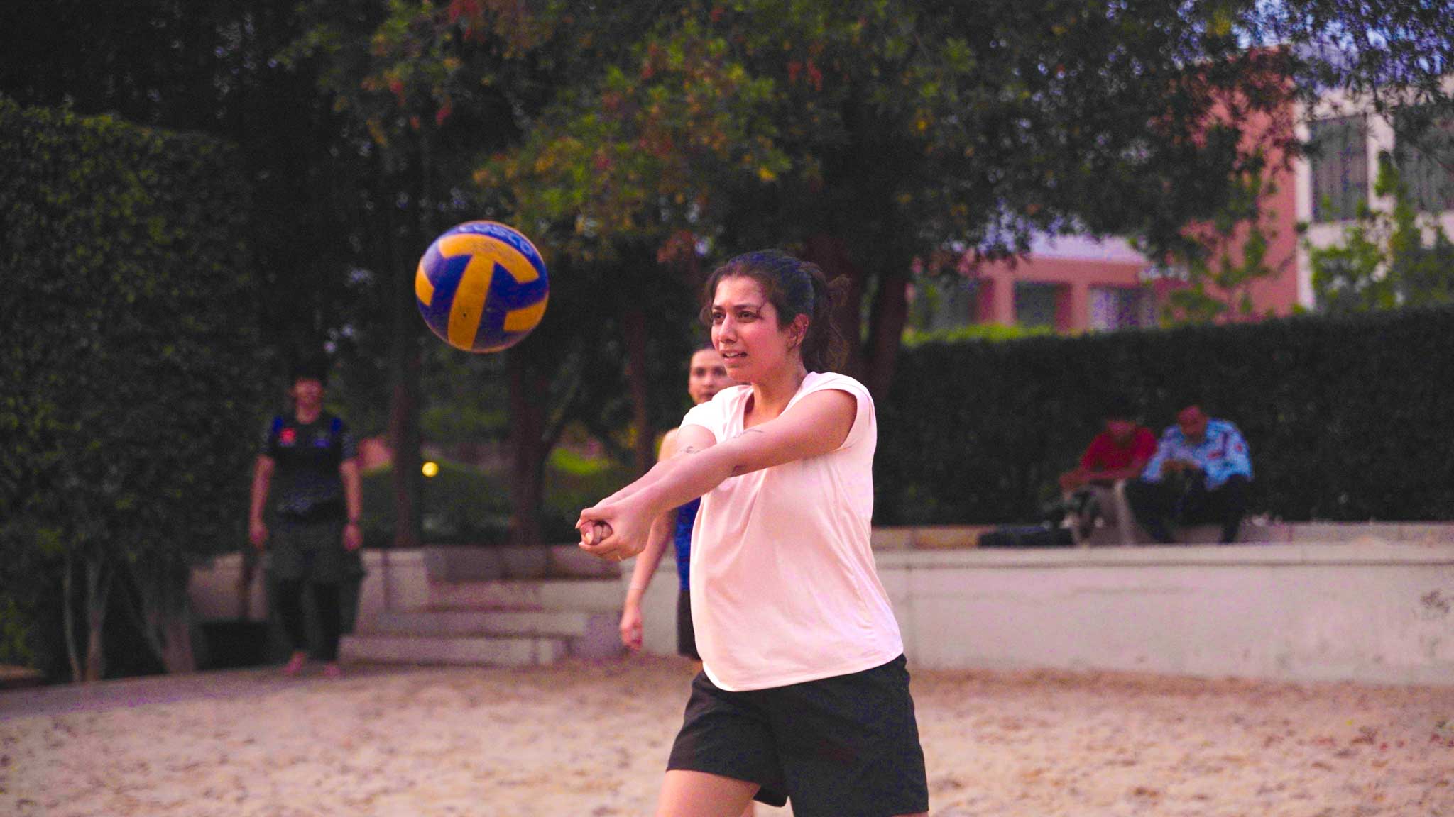 Woman in action hitting a volleyball on a beach volleyball court with spectators seated behind.
