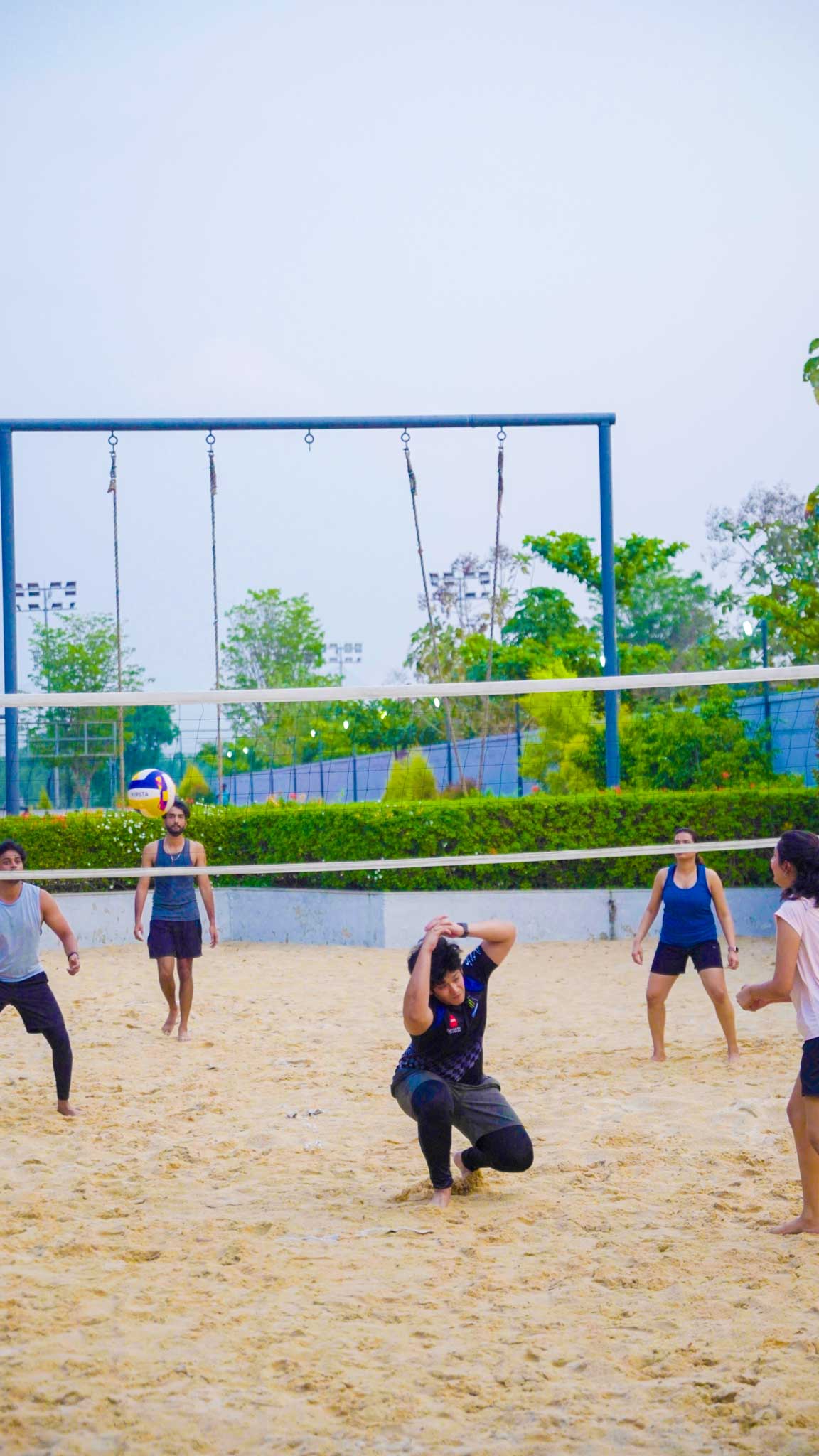 Group playing beach volleyball with one player ducking to avoid the ball on the sandy court.