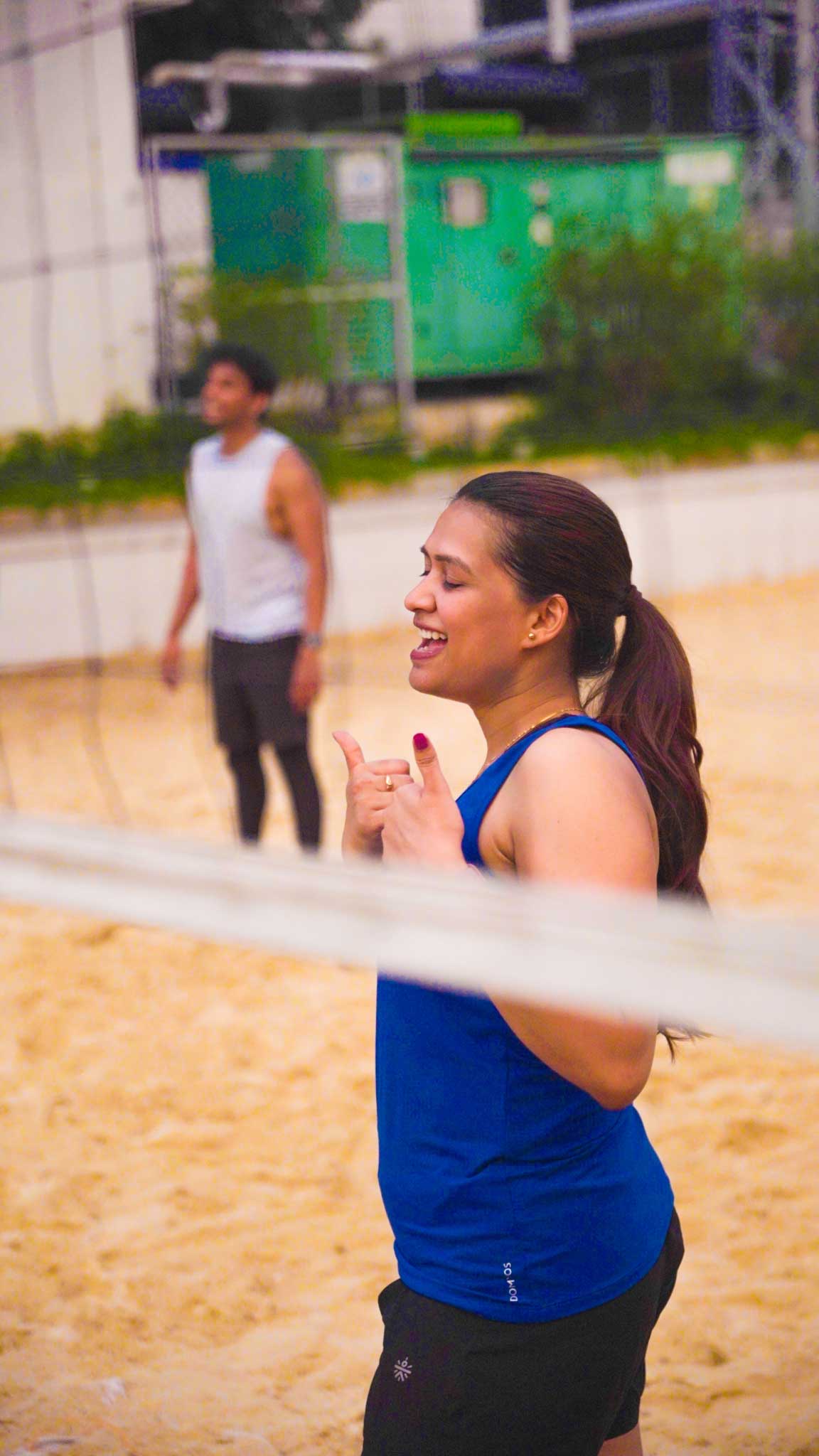 Woman cheering and enjoying the beach volleyball game with players in background.
