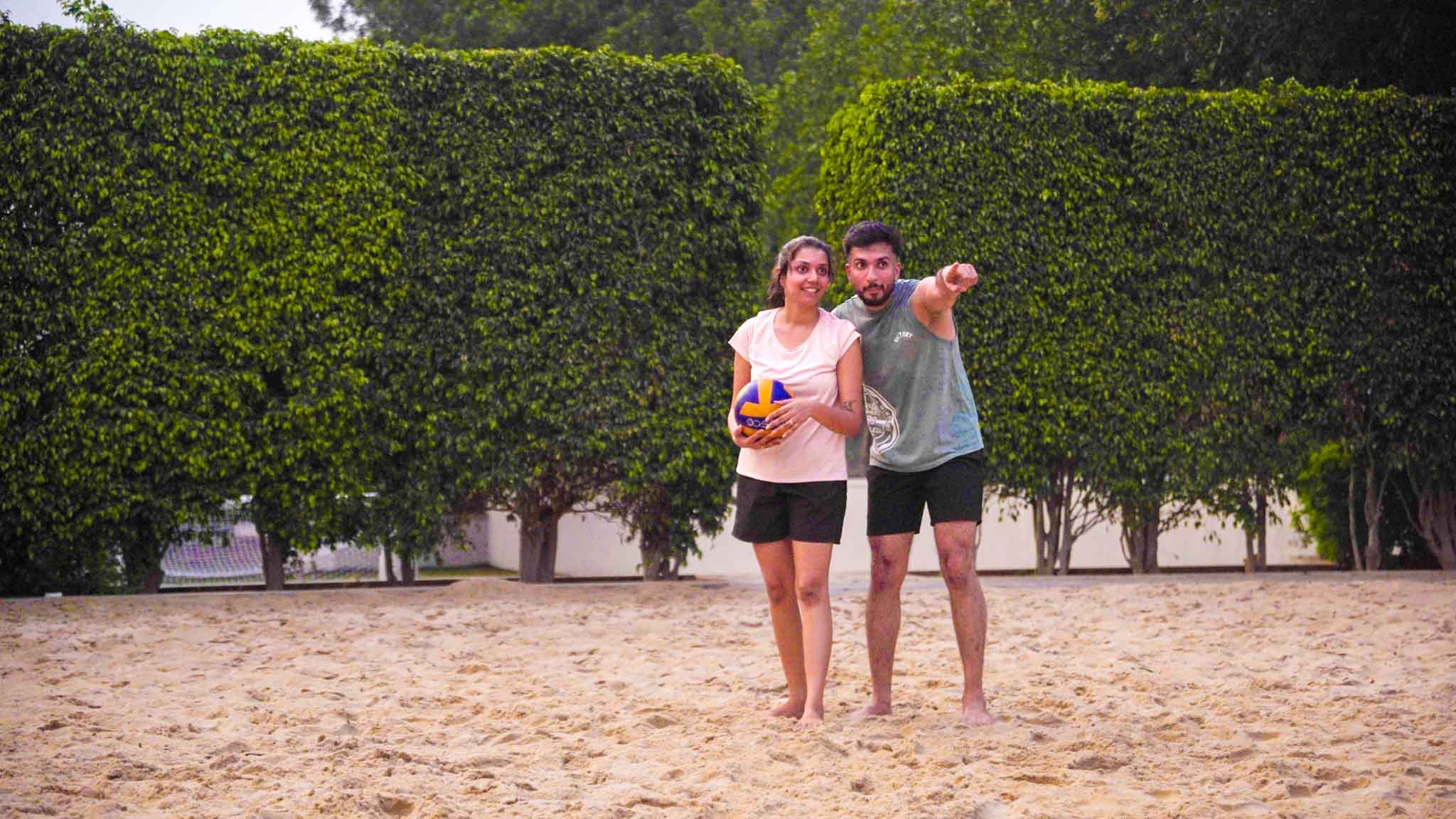 Man pointing and instructing woman holding volleyball on the sandy volleyball court.