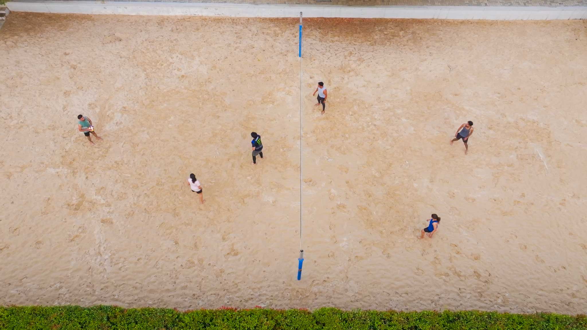 Vertical view of beach volleyball match in progress with players ready on sandy court.