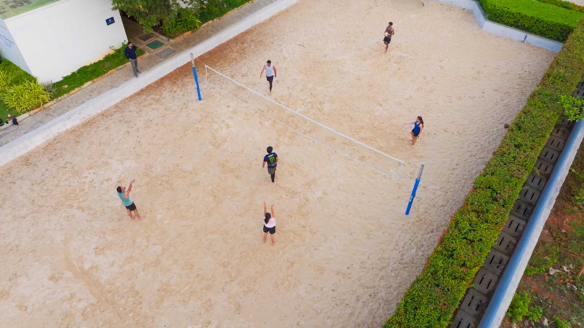 Aerial view of people playing beach volleyball on a sand court surrounded by greenery.