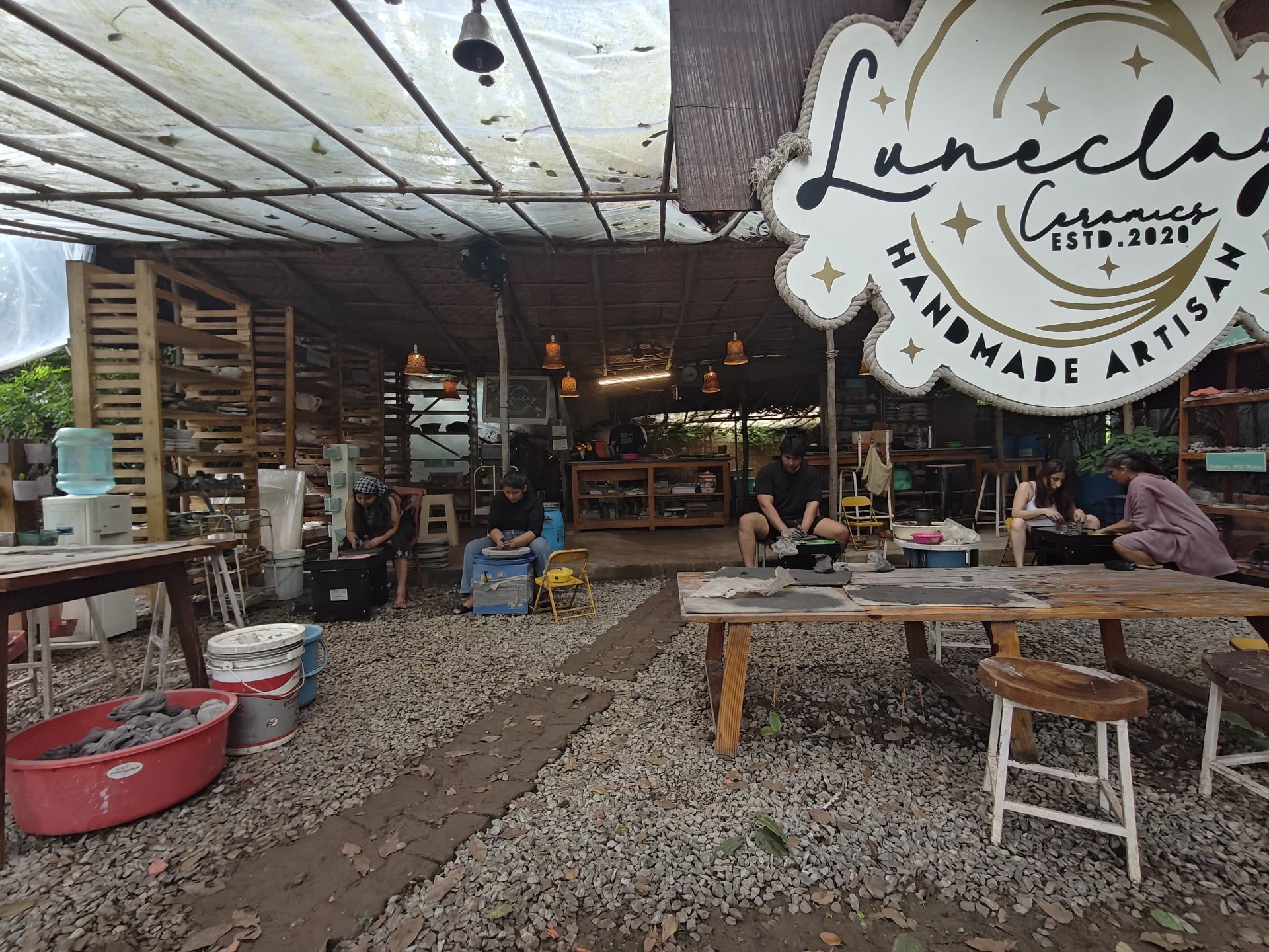 Wide image of the open-air ceramics studio with artisans working on clay projects.