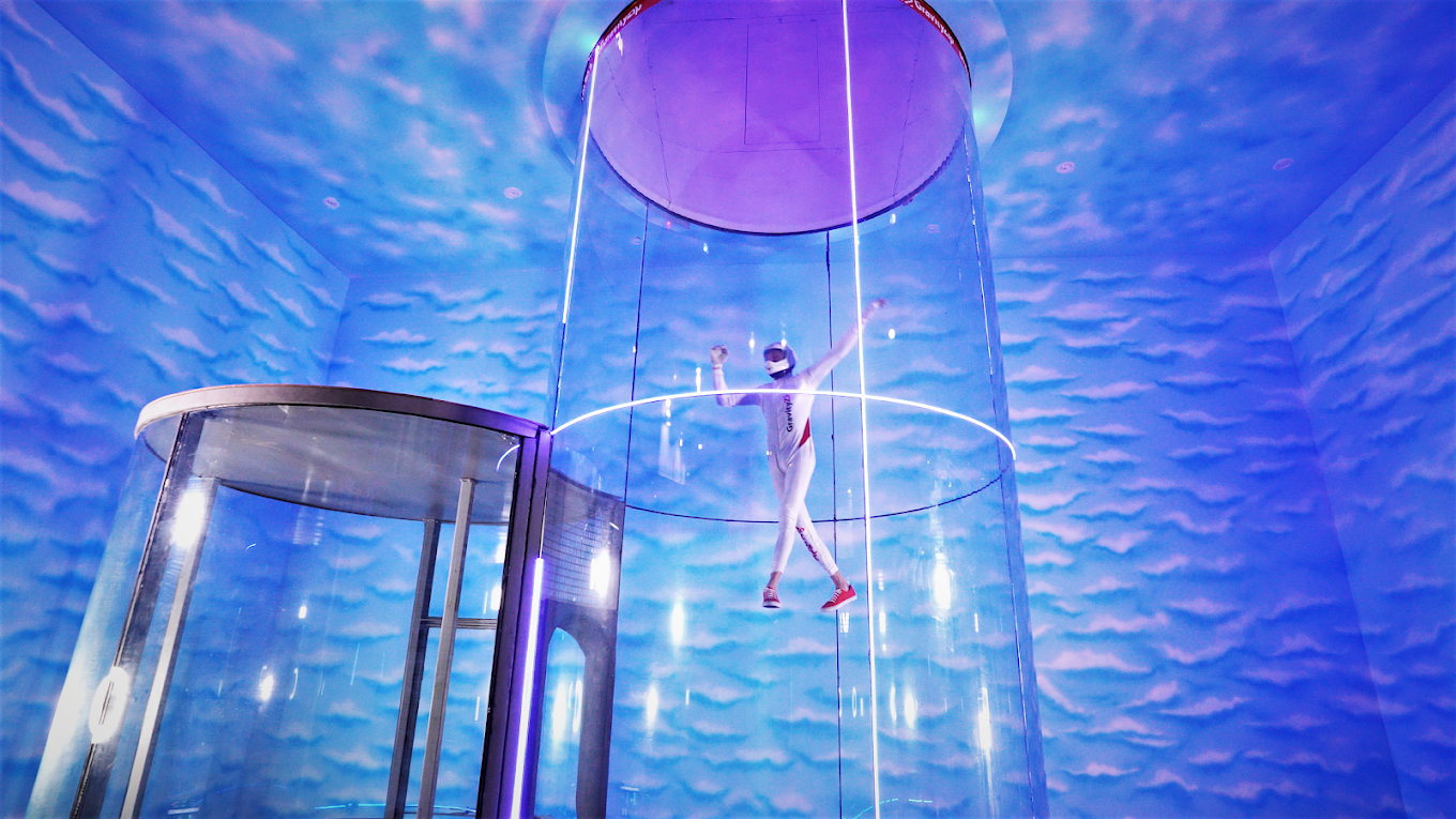 Person flying inside vertical wind tunnel with lit circular lights around the chamber.