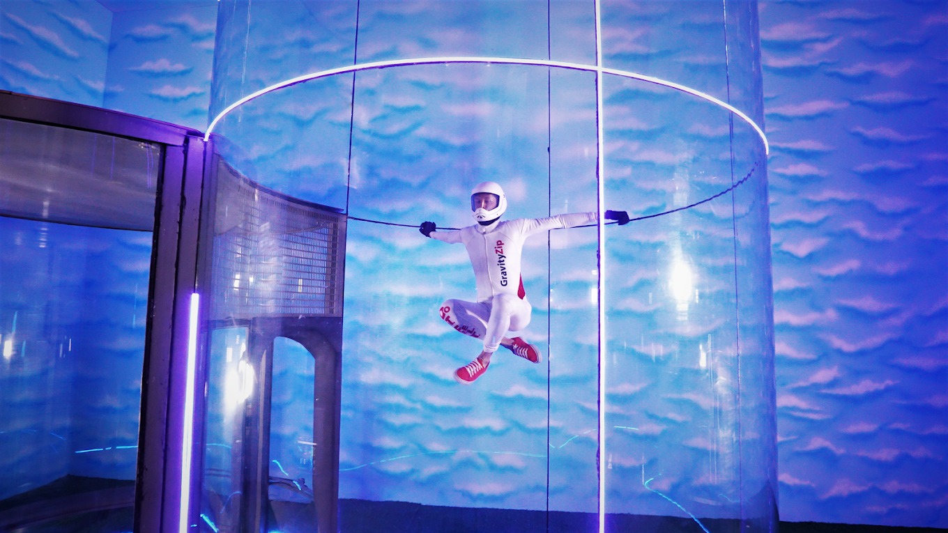 Indoor skydiver performing a pose with arms outstretched inside vertical wind tunnel at GravityZip.