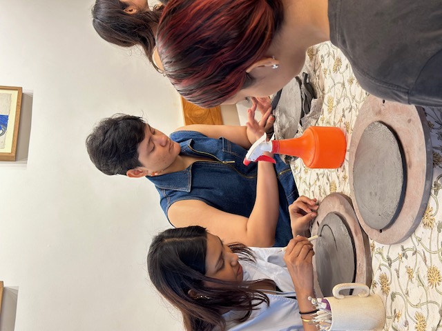 Three women focused on creating their clay trinket dishes at a communal crafting table with tools and a spray bottle.