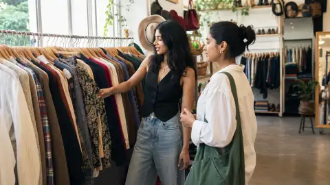 Gallery scene: a candid styling discussion beside a rack, one person pointing at textures while.