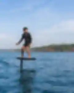 Portrait thumbnail: a single rider on an eFoil board at lift-off on open water, focused.