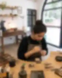 Portrait thumbnail: A focused guest shaping wax for a ring at a tidy workbench, warm studio light,.