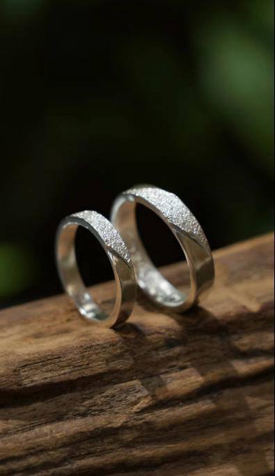 Two textured silver rings placed on a wooden surface showcasing the final handcrafted design.
