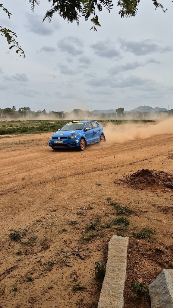 Blue rally car driving aggressively on dry dirt ground, throwing up a trail of dust during the drive.